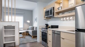 A modern kitchen with built-in appliances, a dining area with a sofa, and a wooden bookshelf. - Towneplace Suites by Marriott Brunswick (Brunswick)