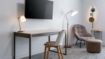 A modern room with a flat-screen TV, a desk, a chair, a floor lamp, and a round table.
