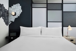 Una habitación de hotel moderna con una cama bien hecha, una mesita de noche con lámpara y un adorno en la pared.
