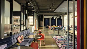 A modern lounge area with a sofa, tables, and chairs, featuring a patterned rug and a view of the cityscape.
