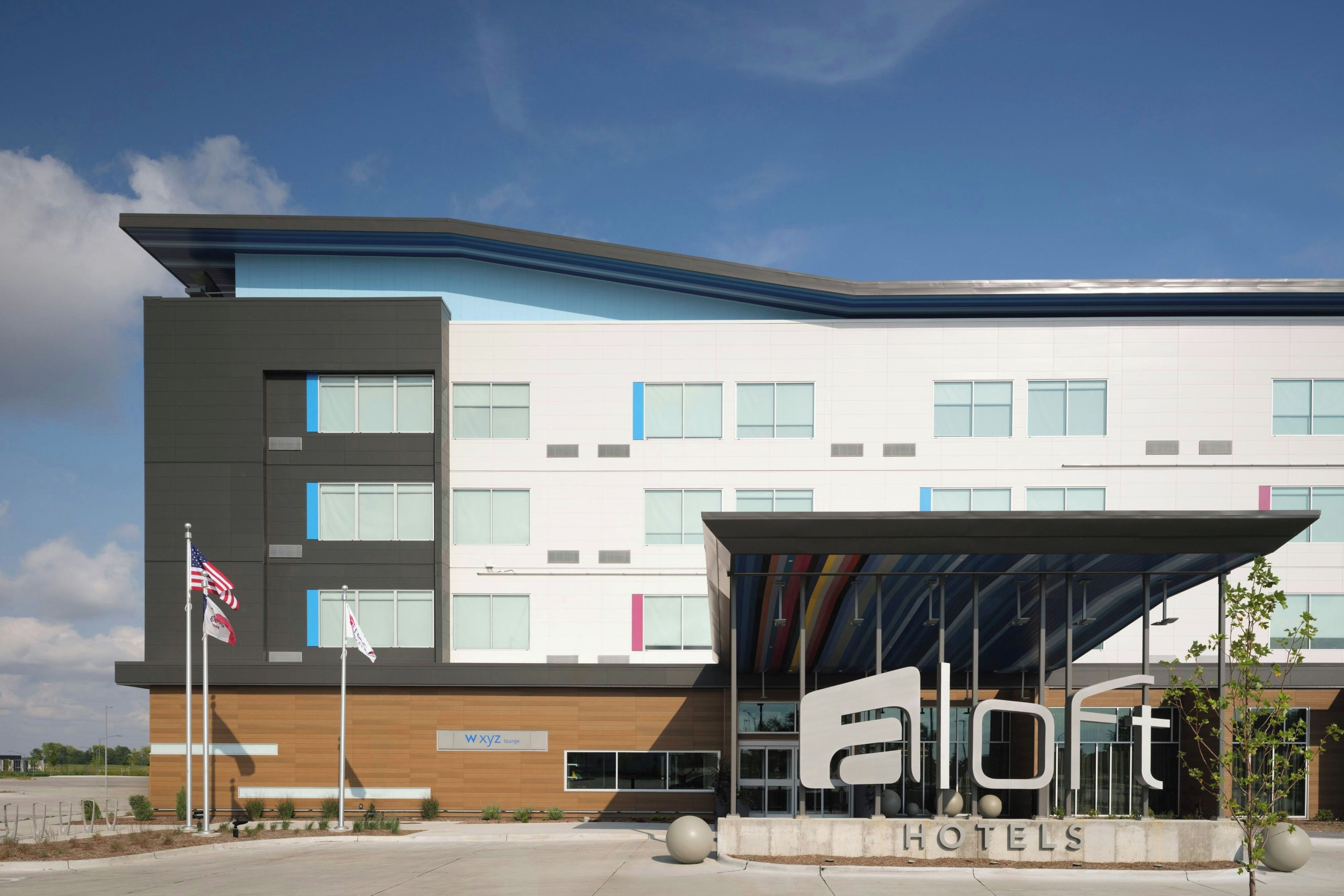 A modern hotel building with a flat roof, multiple windows, and a covered entrance area.