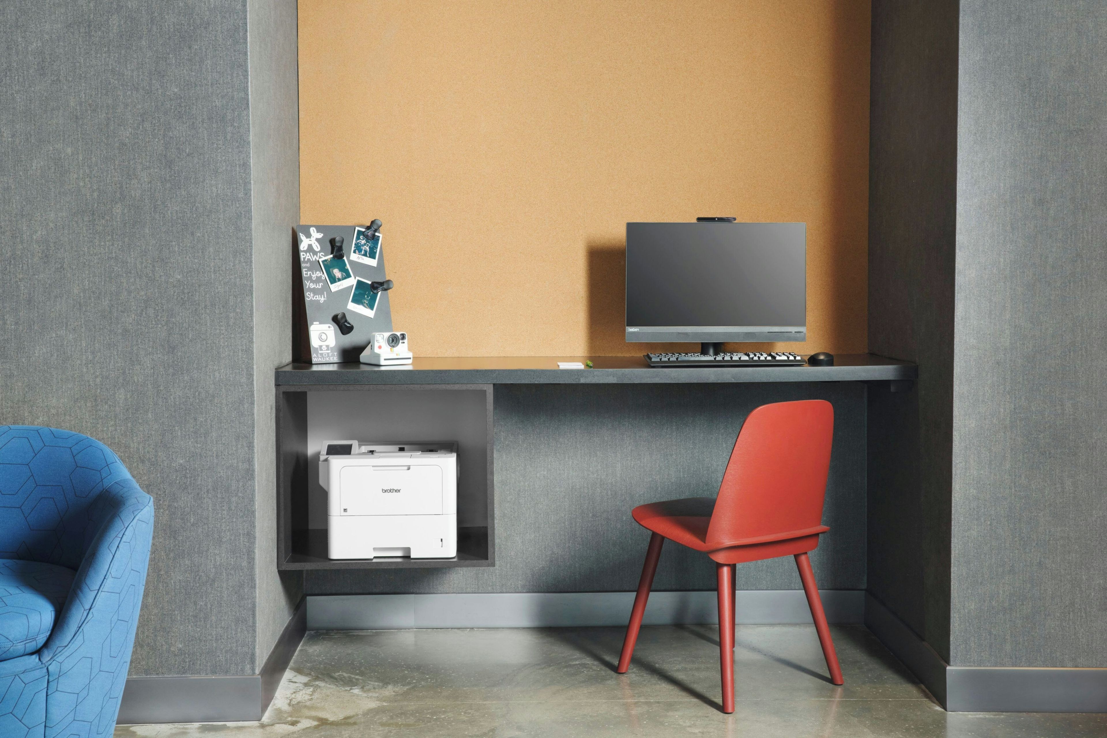 Un escritorio moderno con un monitor de computadora, una impresora y una silla.
