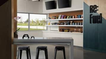 Una cocina moderna con encimera blanca, taburetes negros y vistas a una zona residencial a través de amplios ventanales.