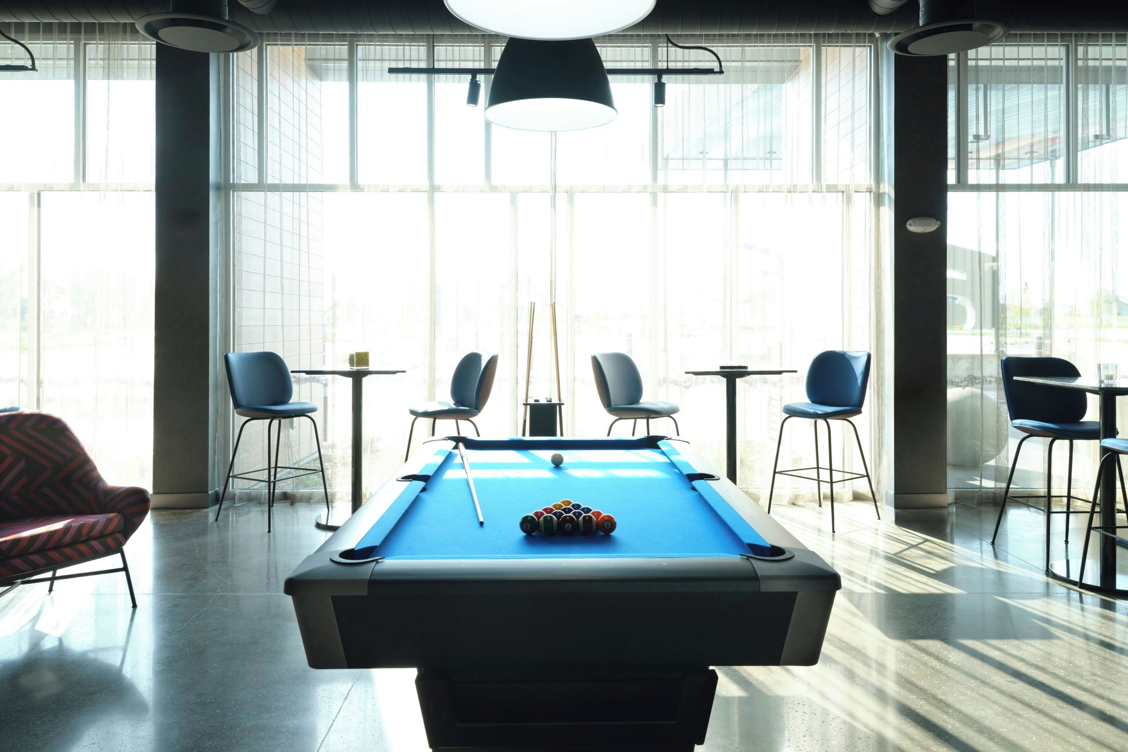 A pool table in a room with large windows, chairs, and tables.