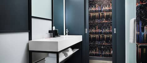 A modern bathroom with a white sink, black shelving, and a cityscape mural on the wall.