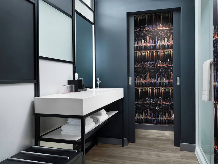 A modern bathroom with a white sink, black shelving, and a cityscape mural on the wall.