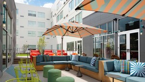 Un área de estar exterior moderna con un sofá modular, sillas verdes y un gran paraguas a rayas.