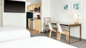 Une chambre d’hôtel moderne équipée d’un lit, d’un bureau avec deux chaises, d’une télévision à écran plat, d’un four à micro-ondes et d’une machine à café.