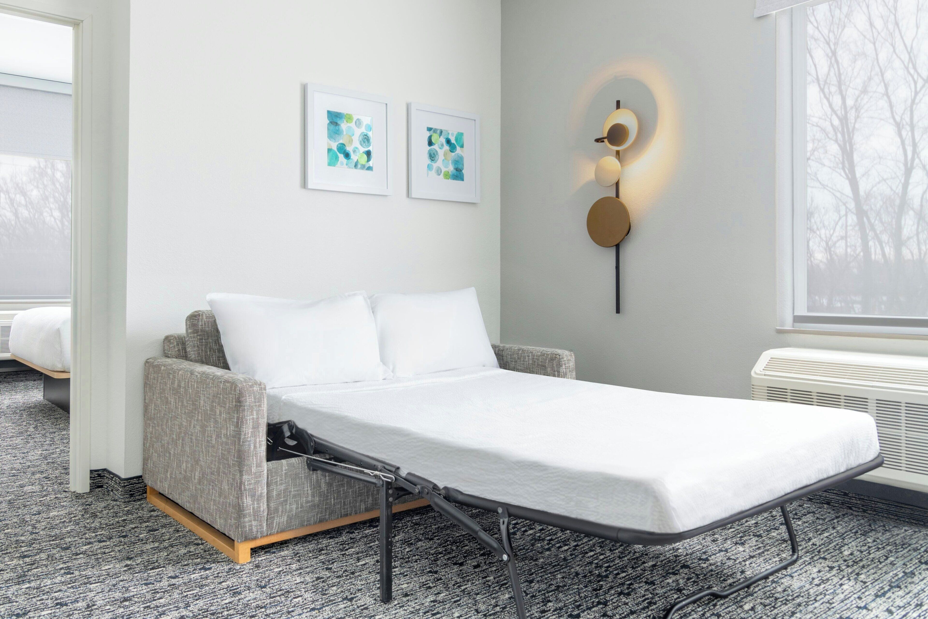 A modern room with a foldable bed, a wall-mounted light fixture, and two framed artworks.