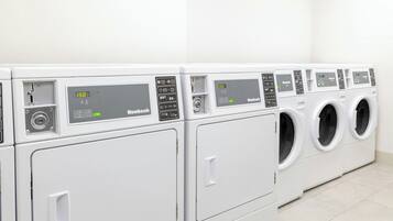 Une rangée de machines à laver modernes à chargement frontal, toutes blanches, dans une buanderie propre carrelée.