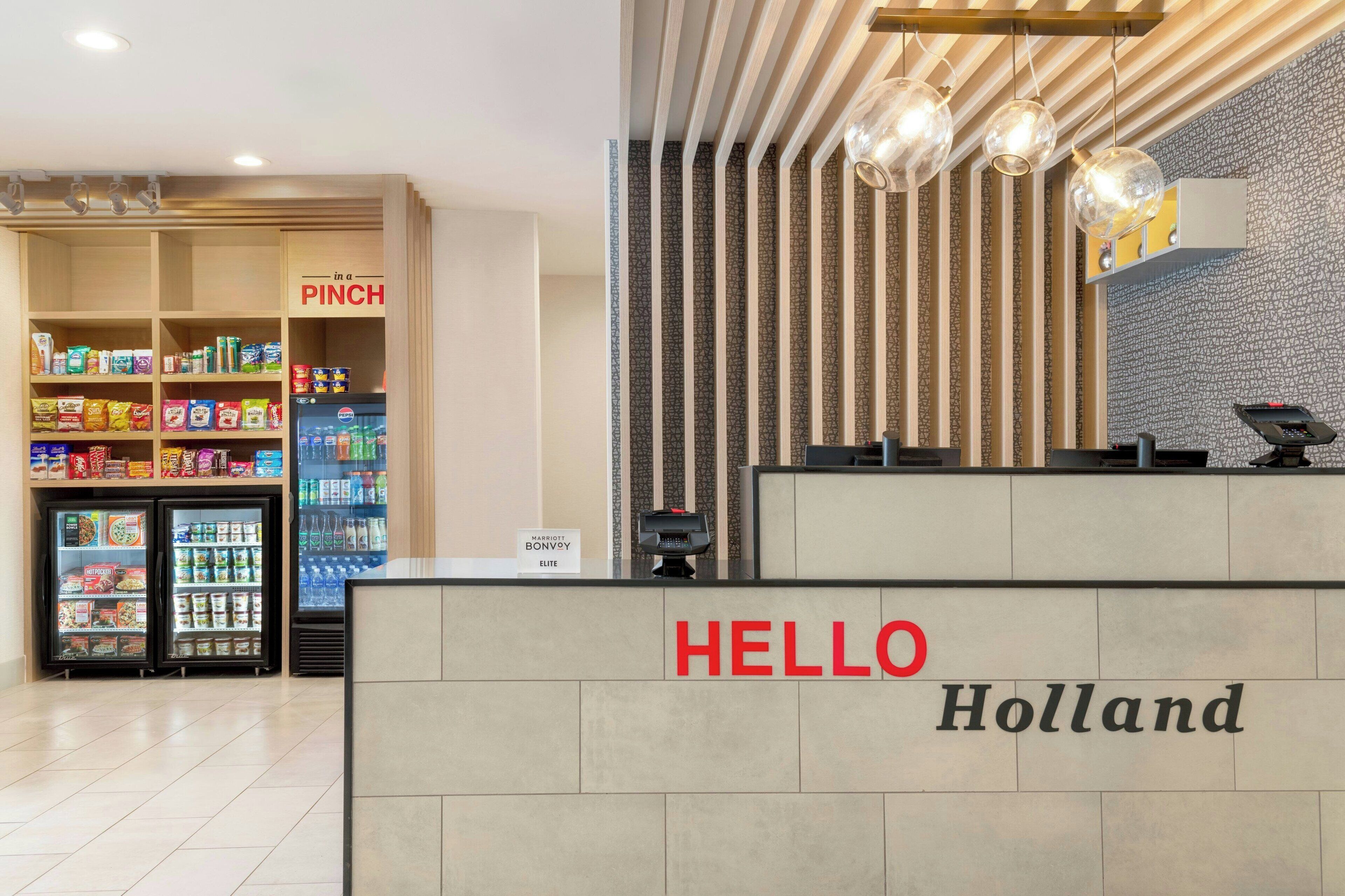 Een hotel receptie met een 'HELLO Holland' bord, een 'PINCH' gekoelde sectie, en een 'Marriott Bonvoy Elite' bord.