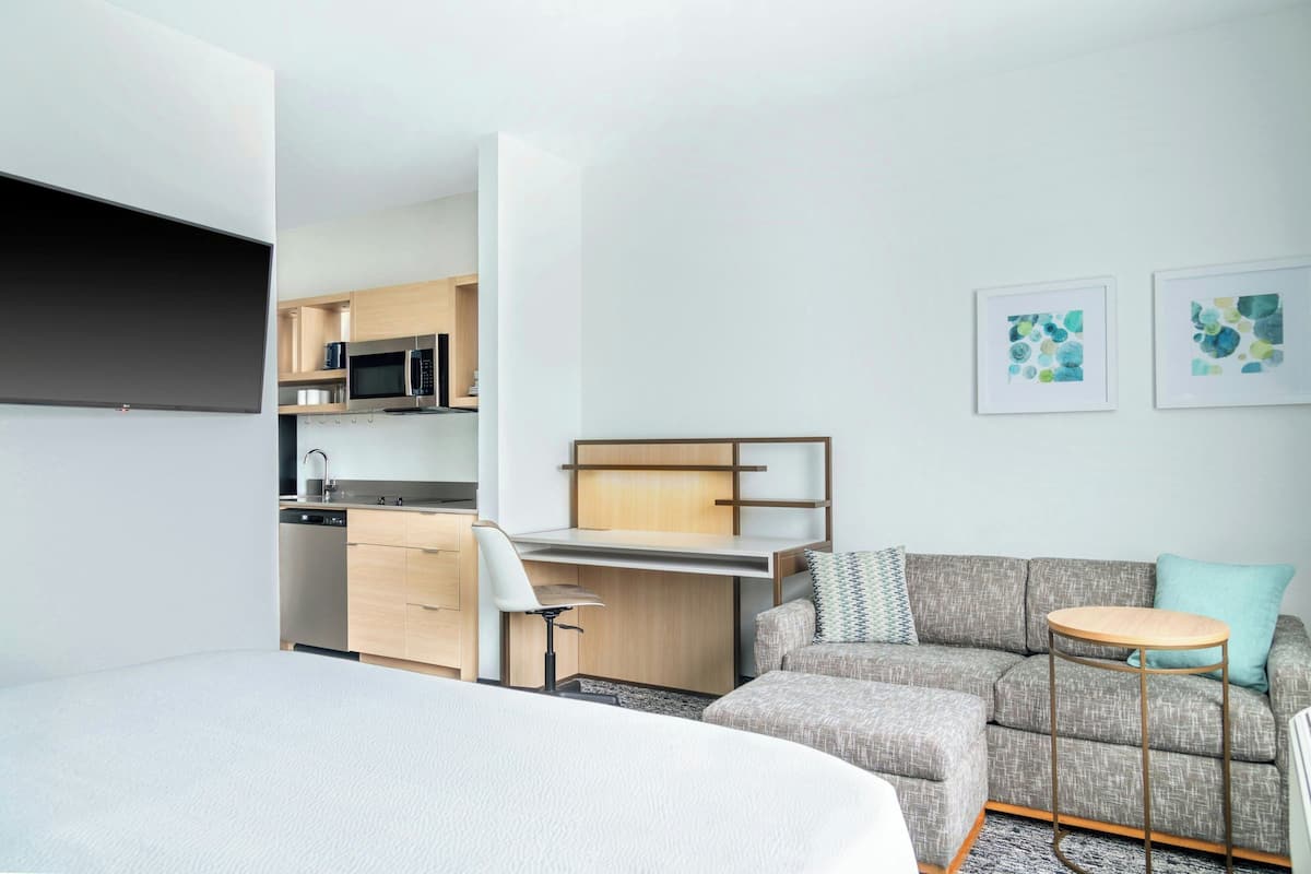 A compact hotel room with a bed, a kitchenette, a sofa, and a small table.