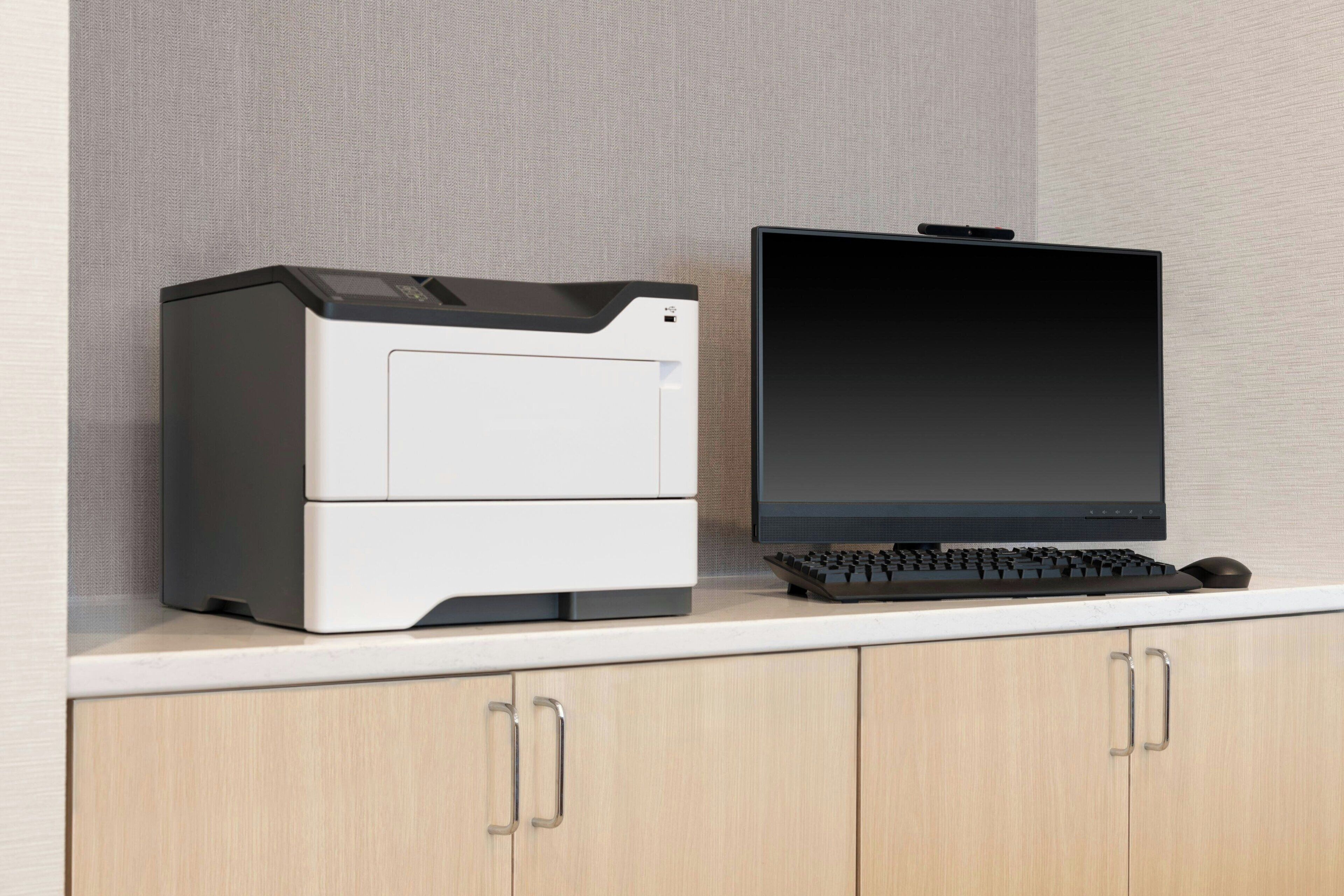 A printer and monitor on a white countertop with wooden cabinets below.
