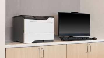 Una impressora i un monitor damunt un taulell blanc amb armaris de fusta sota.