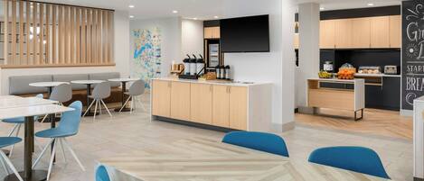 Un comedor moderno con una isla central, diferentes disposiciones de asientos y una zona de cocina con electrodomésticos y un televisor de pantalla plana.