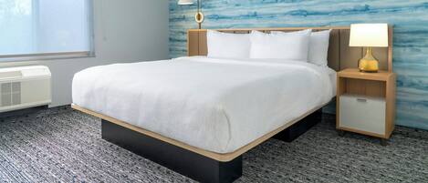 A hotel room with a bed, bedside tables, a lamp, and a window.