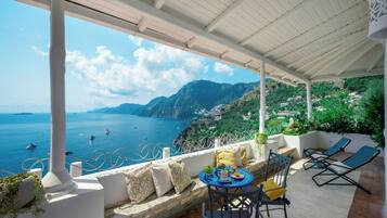 Una terraza con mesa y sillas, con vistas al mar, barcos y montañas.