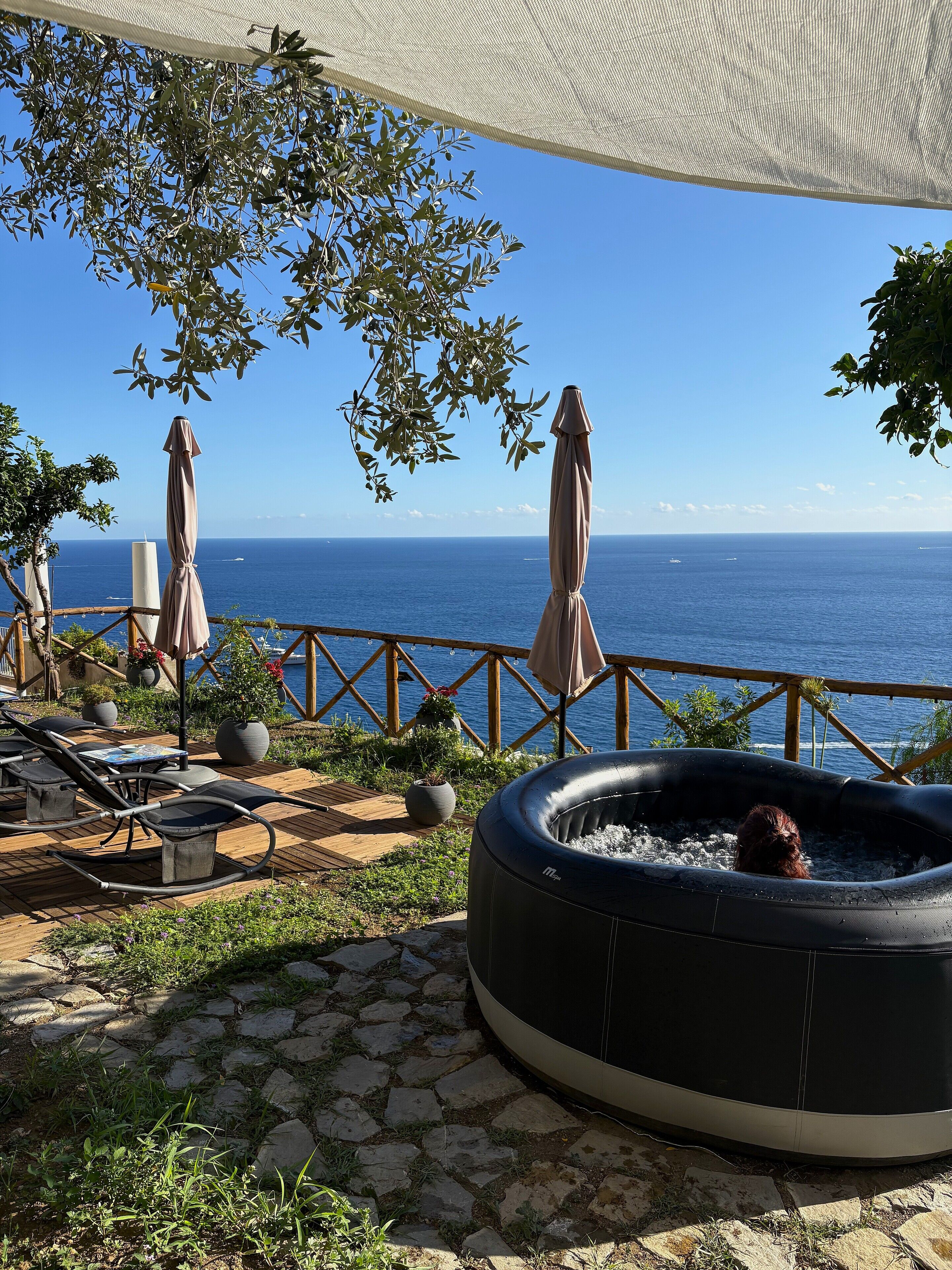 Een terras met een jacuzzi, lounge stoelen en parasols met uitzicht op zee.