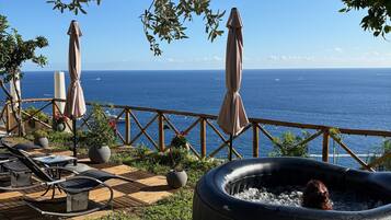 Een terras met een jacuzzi, lounge stoelen en parasols met uitzicht op zee.