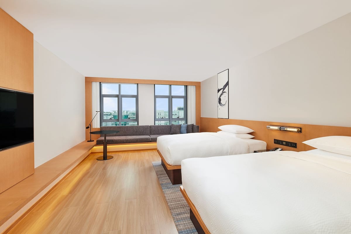 A hotel room with two beds, a TV, a large window with a city view, and a modern design.