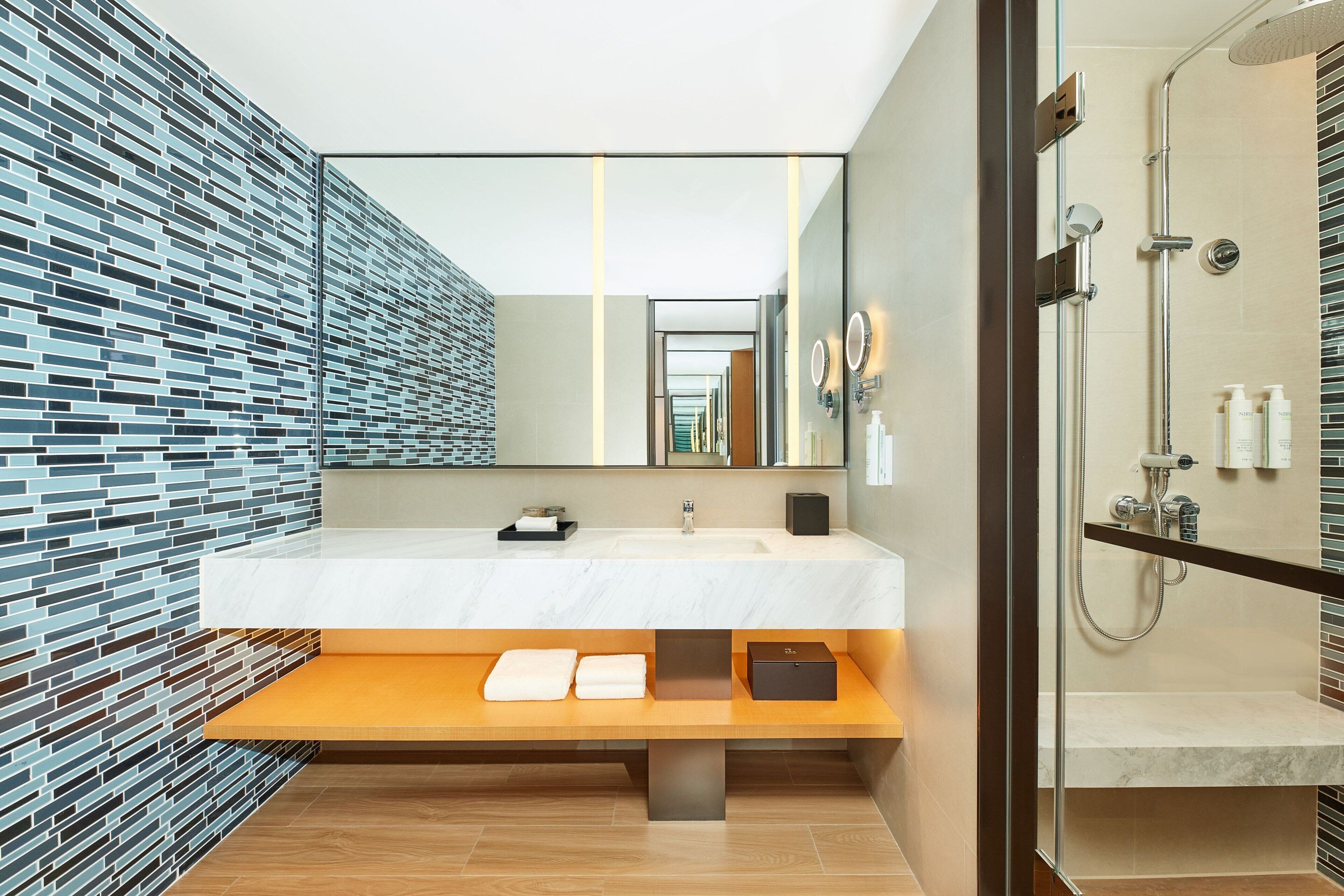 A modern bathroom with a large mirror, a white sink, and a shower area.