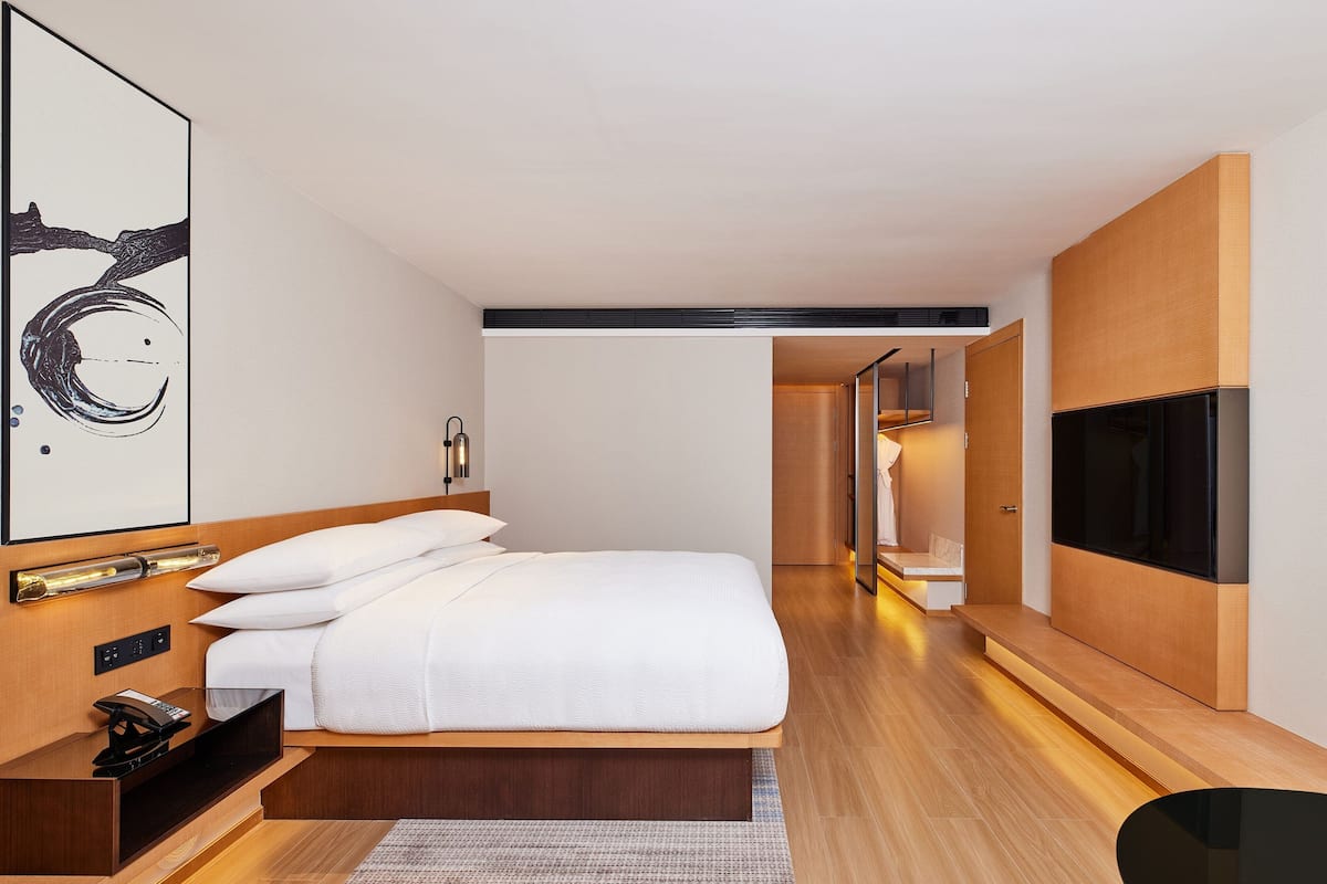 A modern hotel room with a large bed, bedside table, TV, and artwork on the wall.
