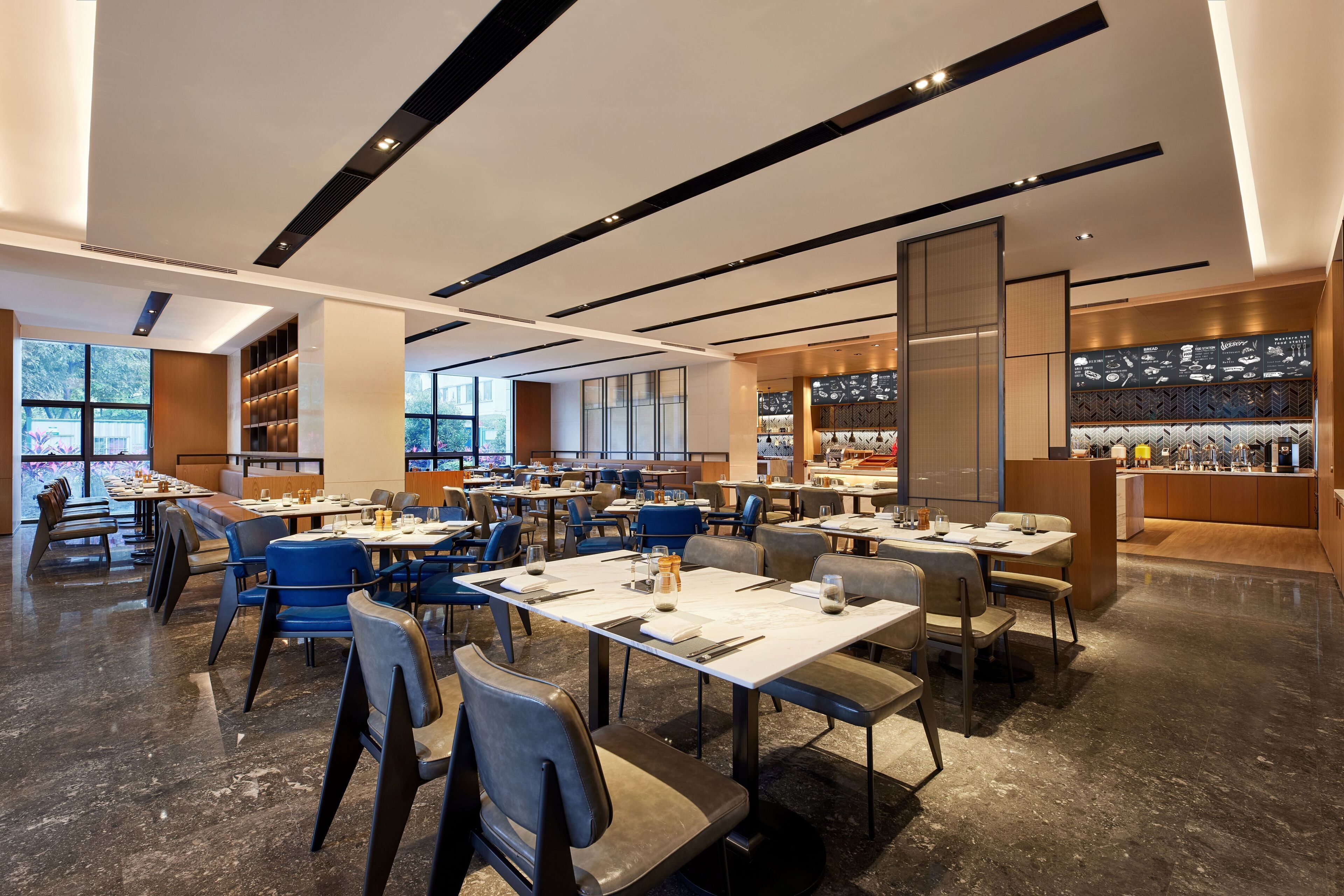 Un restaurante moderno con varias mesas y sillas, ventanas amplias y una cocina visible al fondo.