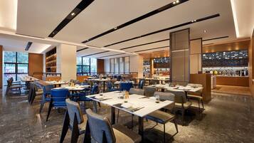 Un restaurante moderno con varias mesas y sillas, ventanas amplias y una cocina visible al fondo.
