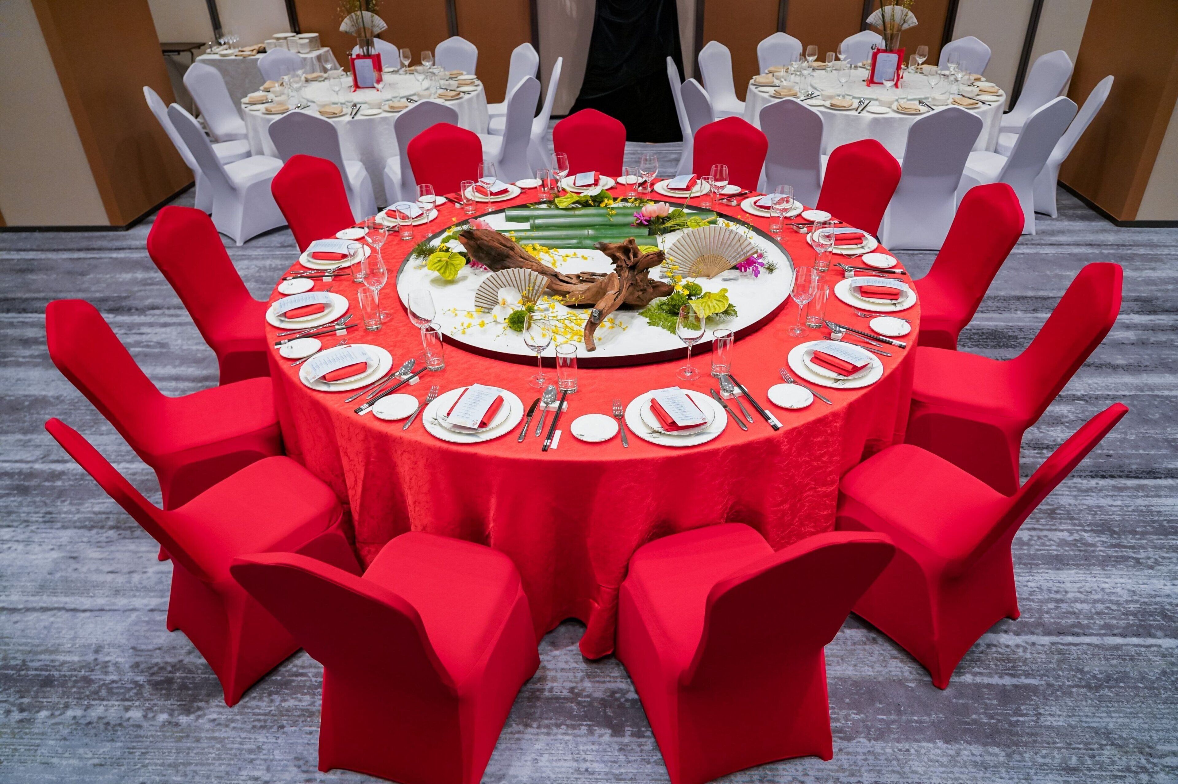 Una mesa redonda con sillas rojas y mantel blanco, rodeada de otras sillas blancas.