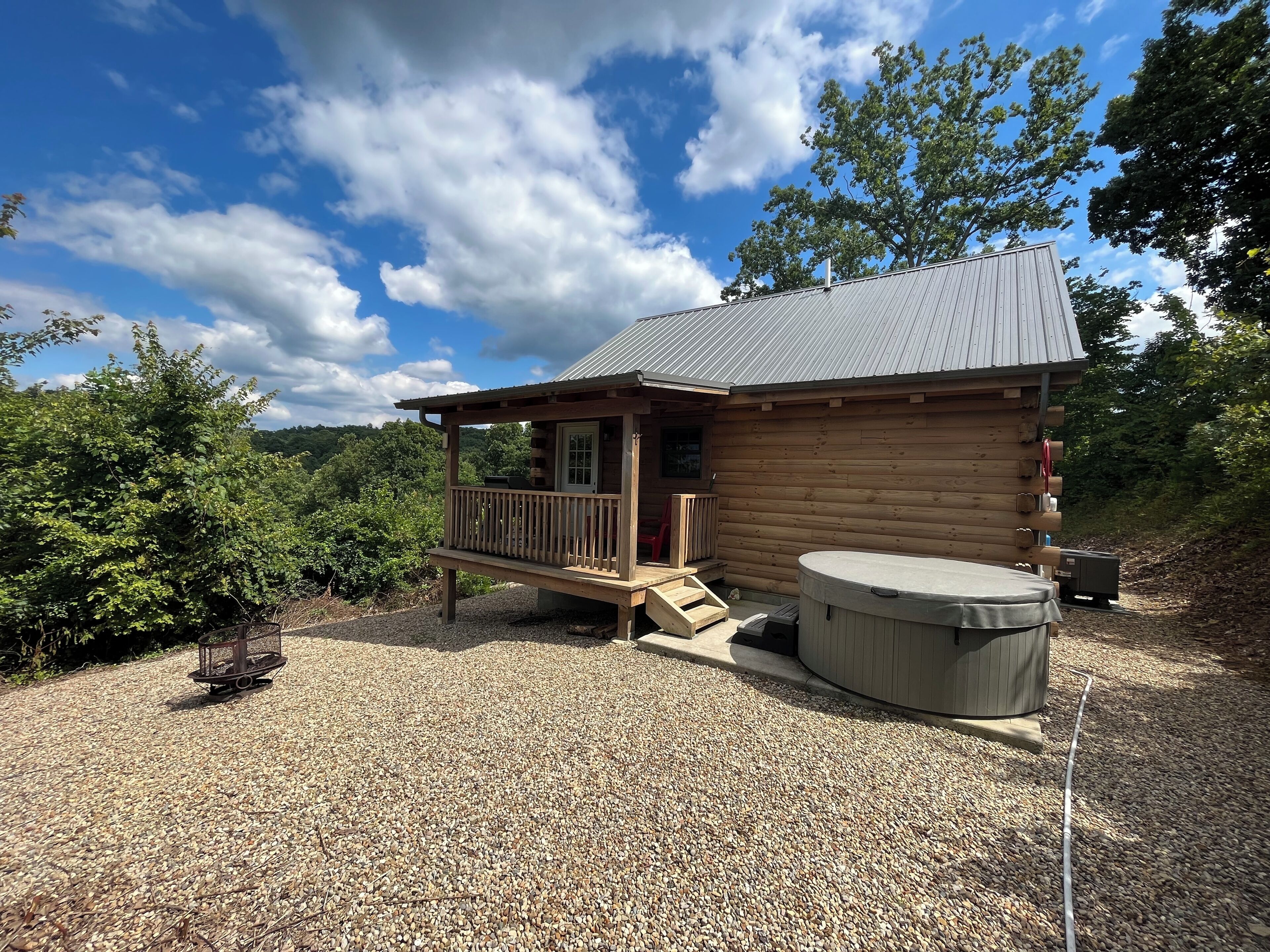 A wooden cabin with a porch, a hot tub, and a gravel driveway.