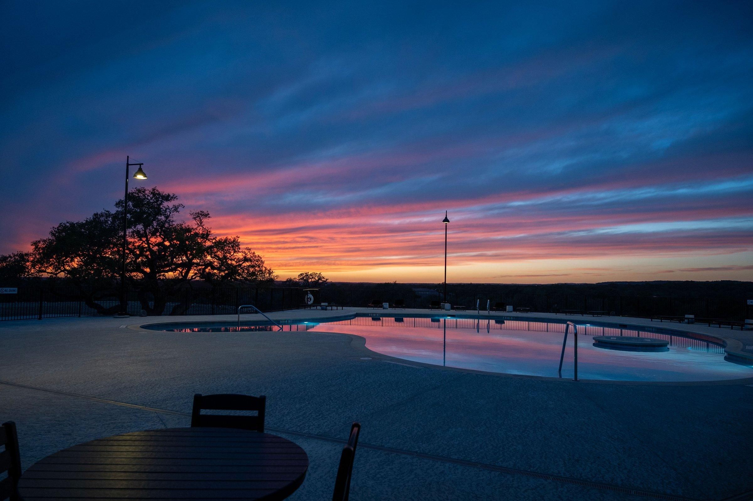 A pool area with a sunset view, a lamp post, and a bench.