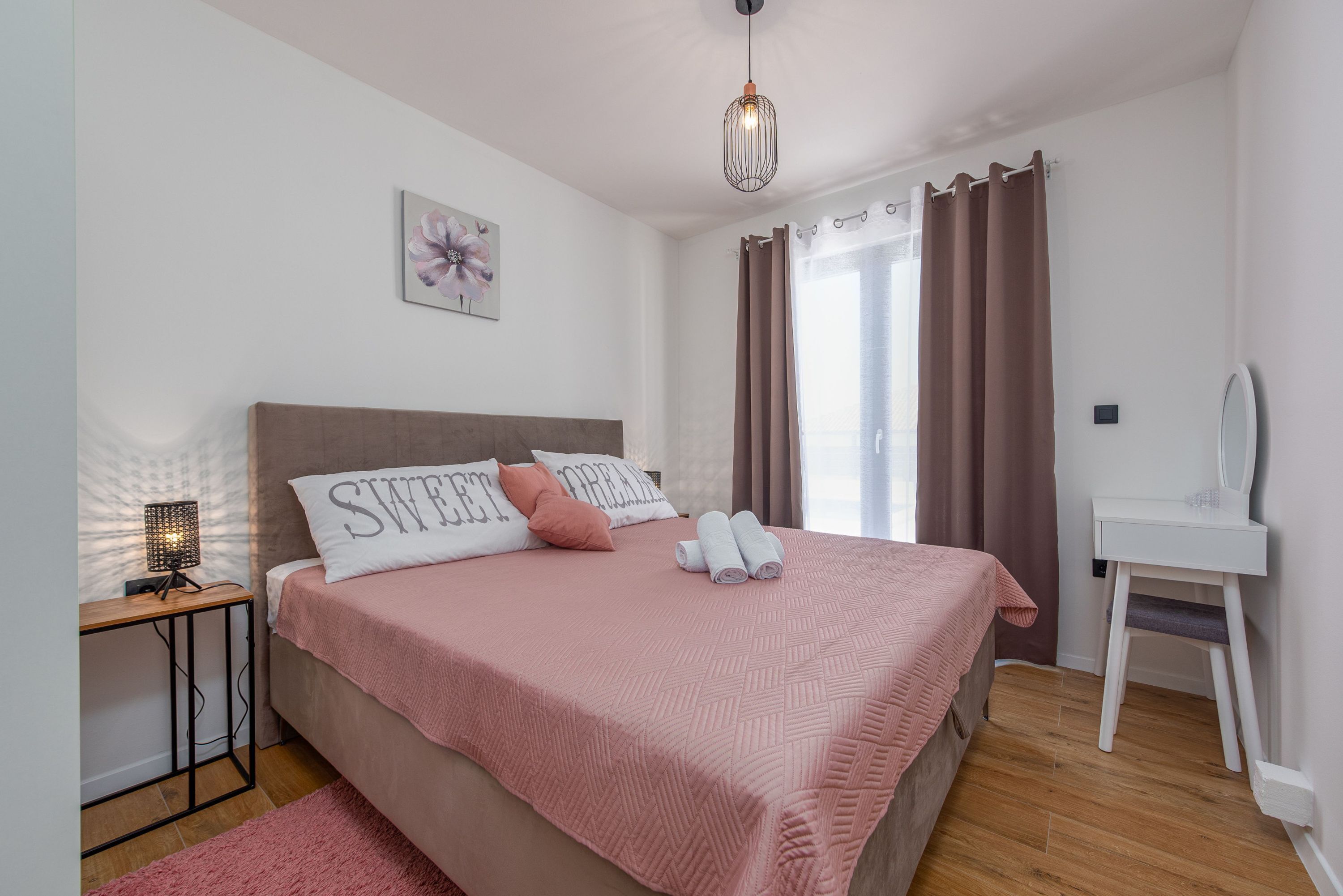 Une chambre bien rangée, avec un lit, une table de chevet dotée d’une lampe, une chaise et une fenêtre avec des rideaux.