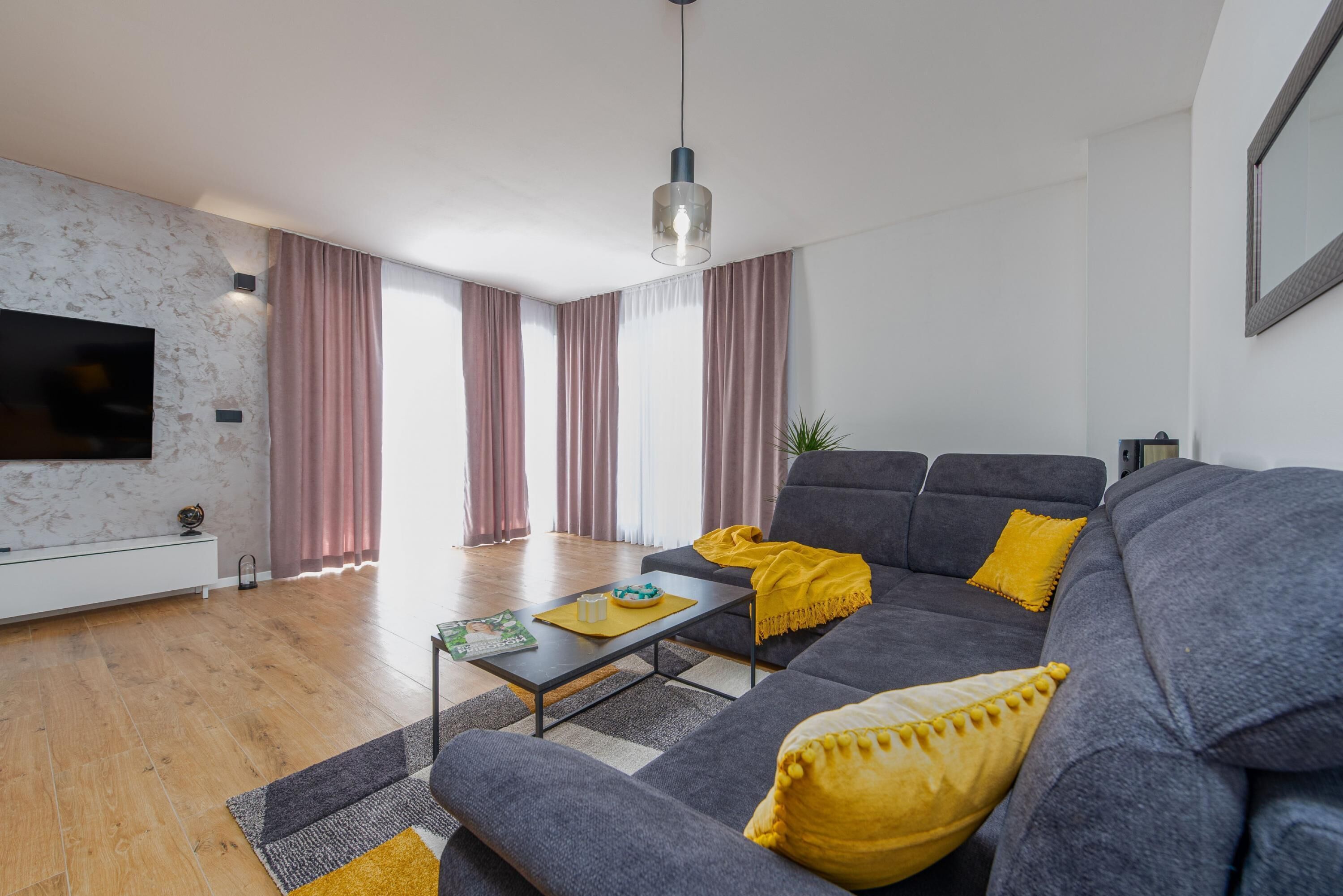 Ein modernes Wohnzimmer mit einem grauen Sofa, gelben Kissen, einem Couchtisch und einem flachbildfernseher, der an einer Marmorwand angebracht ist.