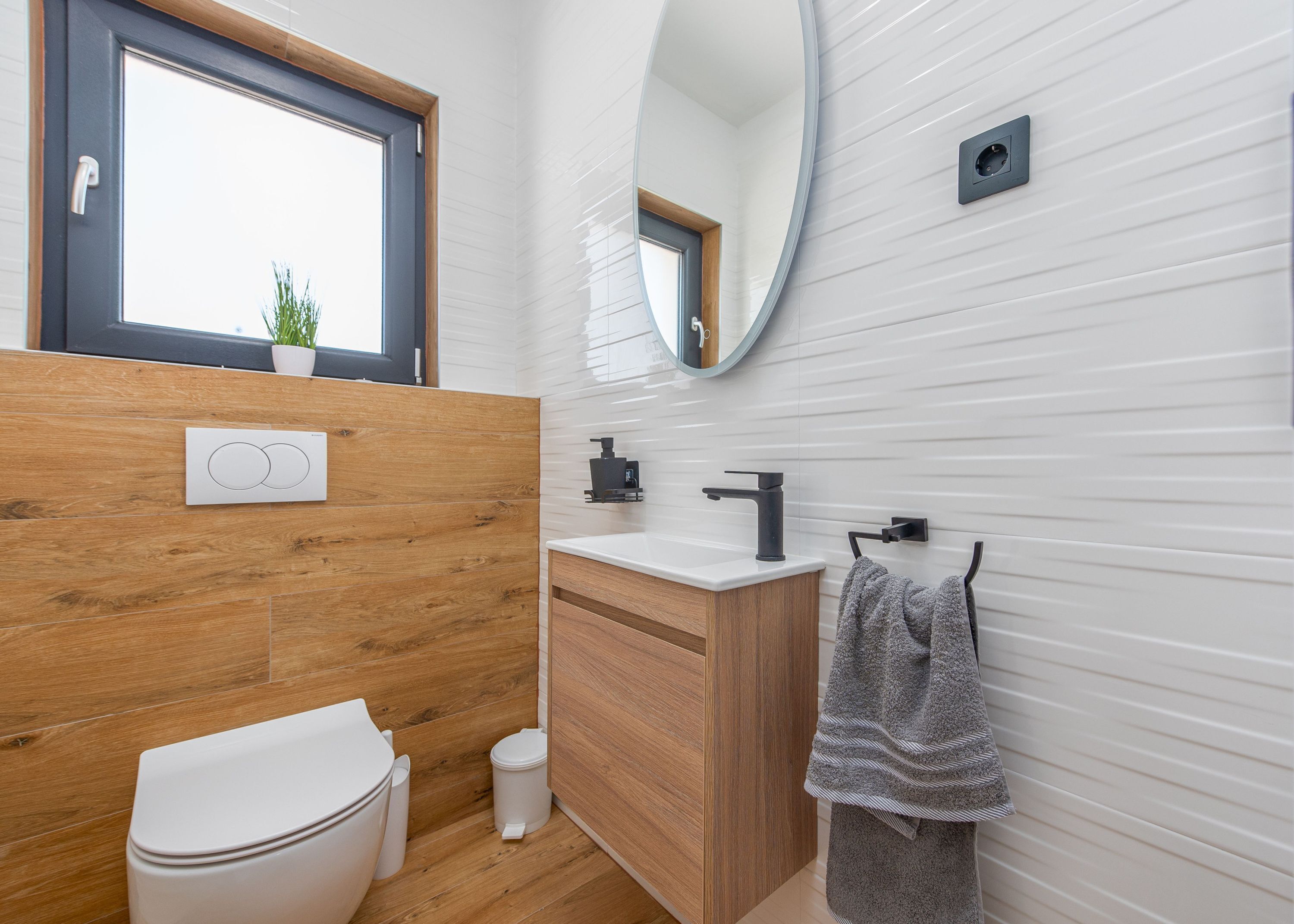 Een moderne badkamer met een houten wastafelmeubel, een wit toilet, een wastafel met een zwarte kraan en een handdoek aan een rek.