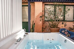 Een bubbelbad met uitzicht op een gebouw, een cactus en een plant in pot.
