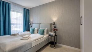 Quarto de hotel moderno com uma cama grande, uma mesa de cabeceira com abajur e vista para a cidade pela janela.