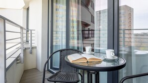 Uma varanda com mesa de vidro, cadeira de vime e um livro.