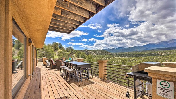 Una terraza de madera con mobiliario exterior y zona de barbacoa, con vistas a un paisaje montañoso.