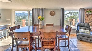 Un comedor con una gran mesa de madera, seis sillas, un jarrón con girasoles y vistas a montañas a través de amplios ventanales.