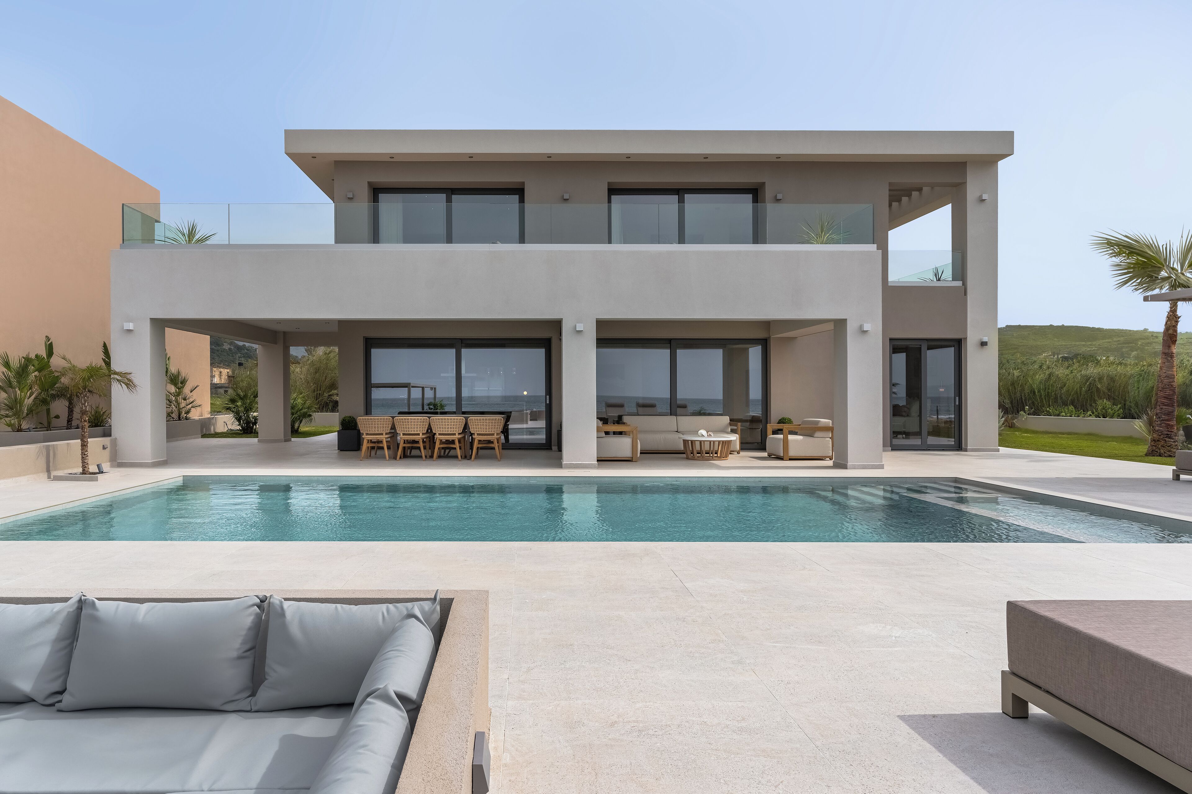 Una casa moderna de dos pisos con piscina, mobiliario exterior y vistas a las colinas.