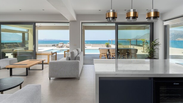 Ein modernes Wohnzimmer mit einem großen Glasfenster, das auf einen Balkon mit Pool und Meerblick führt.