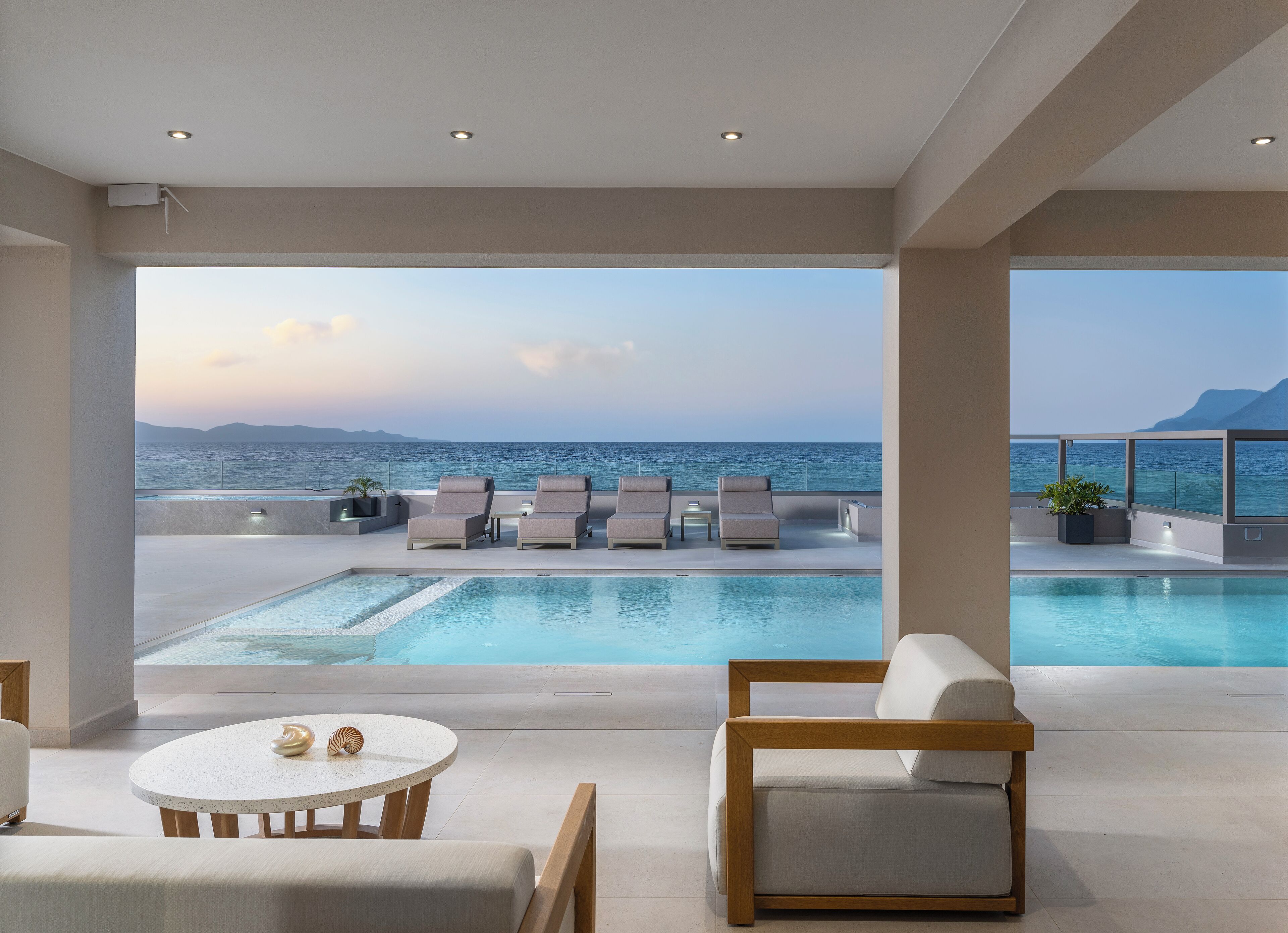 A modern rooftop pool area with lounge chairs and a view of the sea.