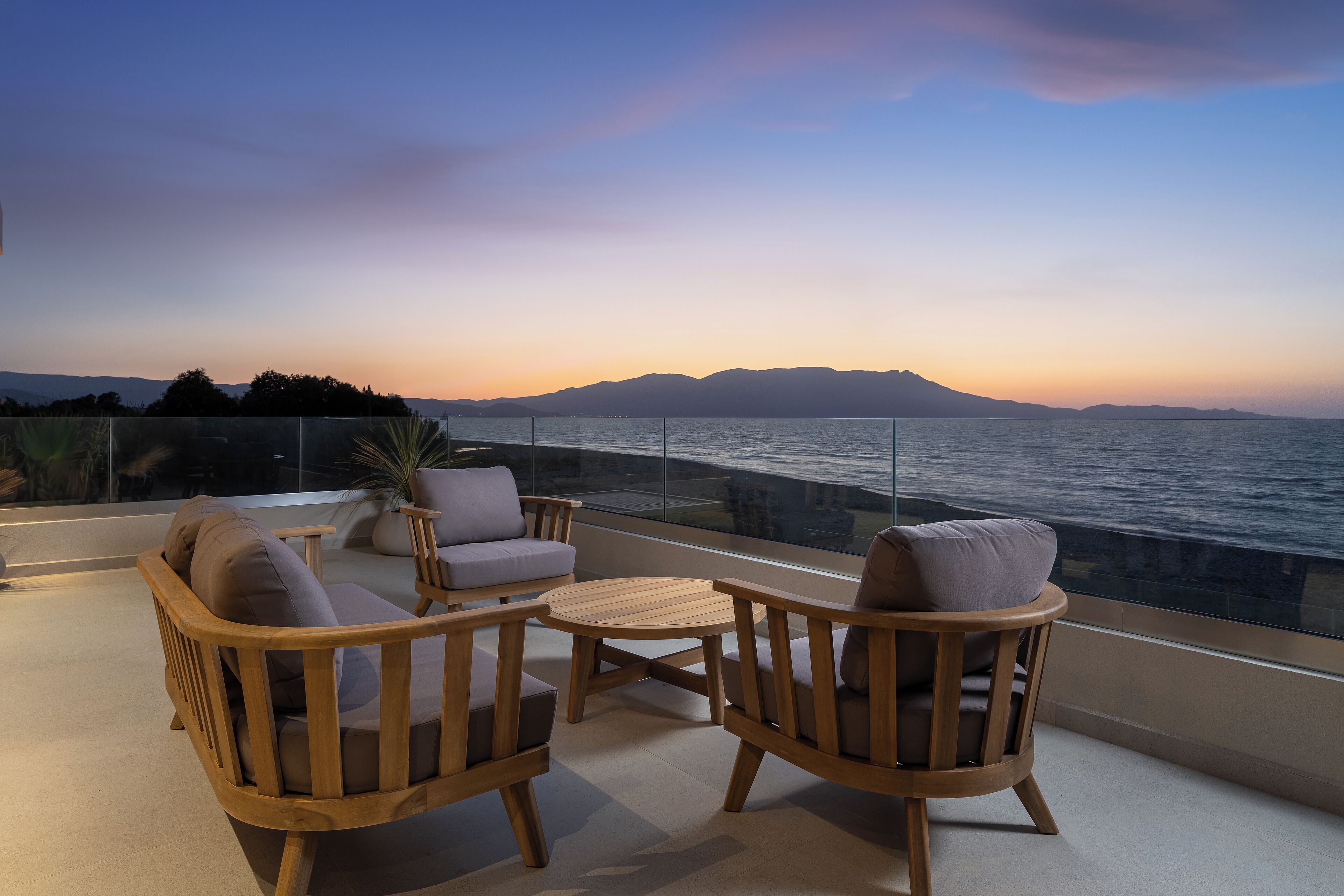 Ein Balkon mit Holzmöbeln und Blick auf das Meer bei Sonnenuntergang.
