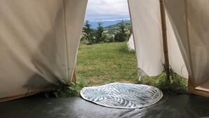 Una estructura tipo tienda de campaña con vistas a un paisaje cubierto de césped y colinas lejanas.