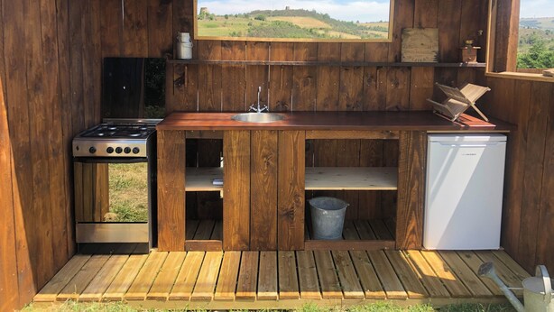 Cocina de madera rústica con estufa a gas, lavaplatos y un refrigerador pequeño.