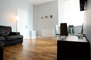 A modern living room with a leather sofa, a dining table with chairs, a radiator, and framed artwork on the wall.