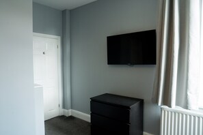 Una habitación con una puerta blanca, un armario negro y un televisor montado en la pared.