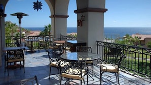 Un patio exterior con mesas y sillas redondas, una decoración colgante en forma de estrella y vista al océano.