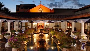 Un patio con una fuente central, rodeado de columnas y plantas en macetas.