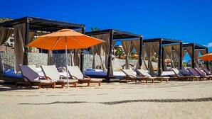 Un área de descanso en la playa con múltiples tumbonas y sombrillas naranjas, frente a un cielo azul despejado.
